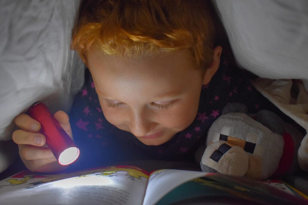 nene leyendo en la cama con una linterna